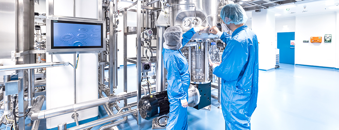 Two people with cleanroom clothing in front of production skid in cleanroom, handling small tubes on a vessel