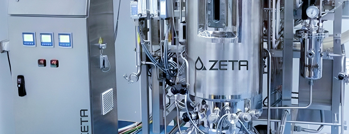 The image shows a large metal tank labeled “ZETA” with pipes, valves, and a control panel nearby. The panel has digital displays and red switches.