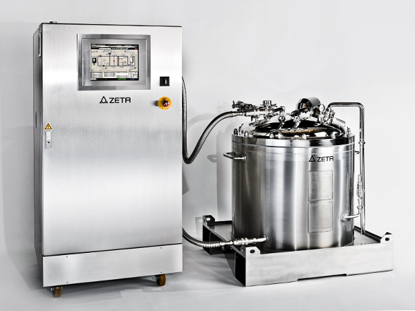 The image shows two pieces of industrial equipment made of shiny metal. One is a control unit with a screen and buttons, including an emergency stop. The other is a large tank with pipes and valves. Both are labeled “ZETA” and used in clean, precise manufacturing settings.
