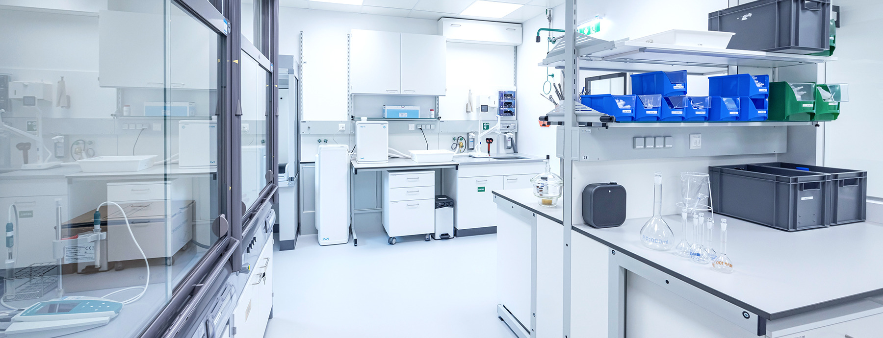 The image shows a professional laboratory with multiple workstations, computers, scientific instruments, and shelves stocked with supplies and chemicals.