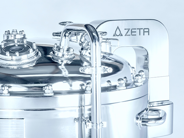 The image shows a close-up of a shiny metal tank with pipes and fittings on top. A metal plate on the tank reads “ZETA.”