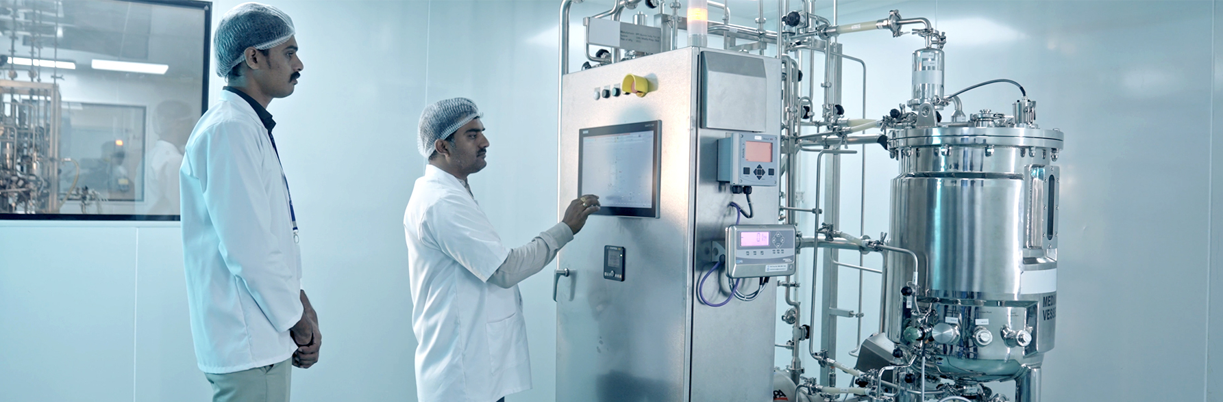 The image shows a clean, modern laboratory with a biosafety cabinet, a central table holding electronic devices and tubing setups, and various cabinets and lab equipment in the background.