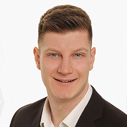 Portrait picture of a person wearing a white shirt and a black blazer in front of a light background.