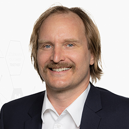 Portrait picture of a person wearing a white shirt and a black blazer in front of a light background.