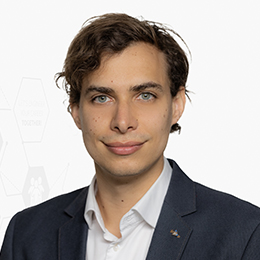 Portrait picture of a person wearing a white shirt and a black blazer in front of a light background.