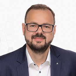 Portrait picture of a person wearing a white shirt and a black blazer in front of a light background.
