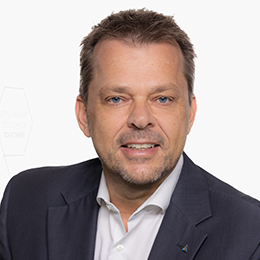 Portrait picture of a person wearing a white shirt and a black blazer in front of a light background.