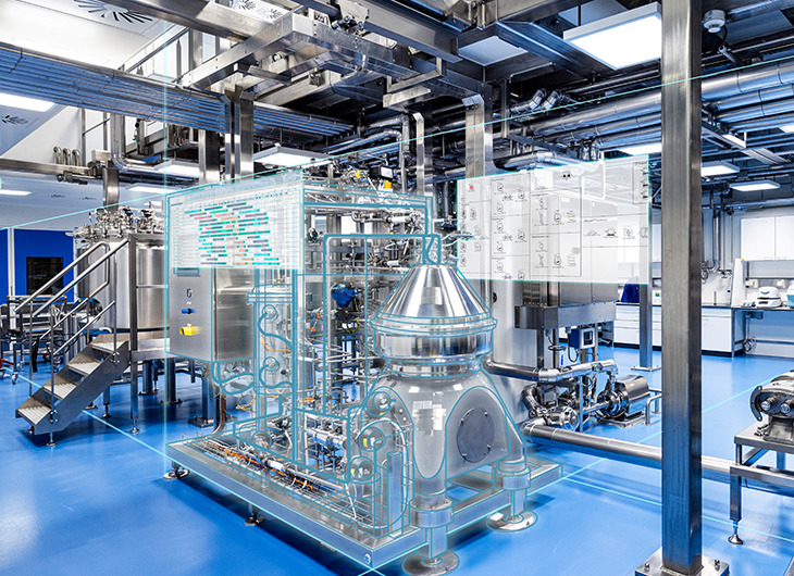 A clean, modern industrial facility with large metal tanks and complex piping. Some equipment has digital overlays, suggesting the use of augmented reality or smart monitoring.