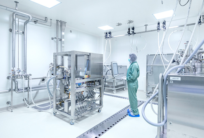 Person in cleanroom clothing in production area, mobile skids connected with hoses to the ceiling